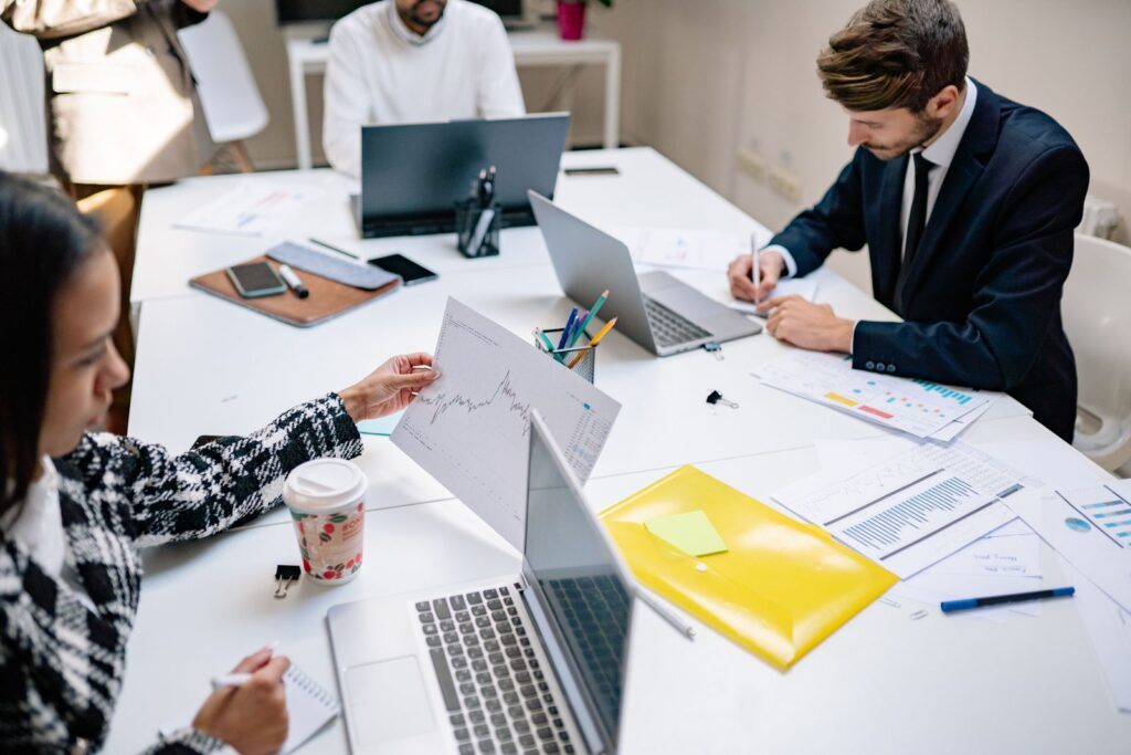 Marketing team reviewing charts and reports on laptops around an office table