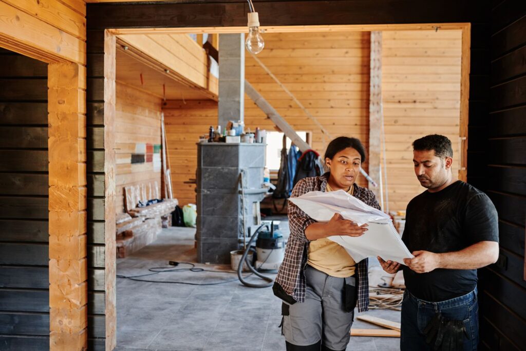 Two builders reviewing printed plans inside a timber house under construction