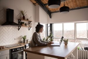 Woman typing a question into a laptop at a kitchen bench to compare AI assistants