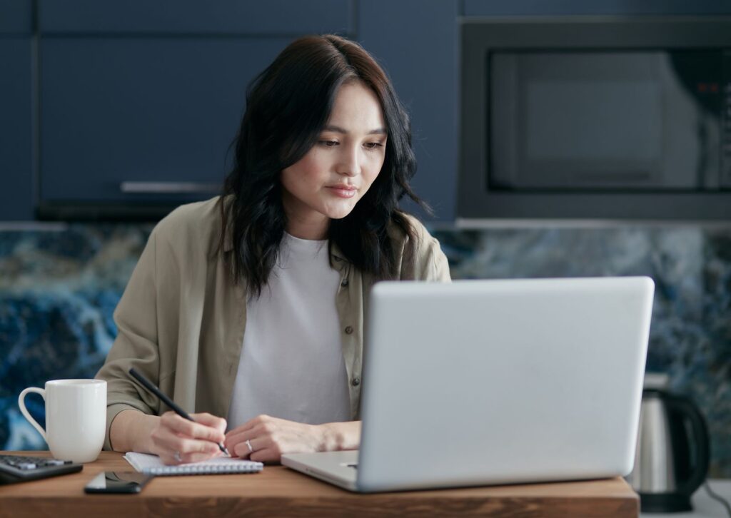 Woman taking notes beside her laptop while comparing answers from different AI assistants
