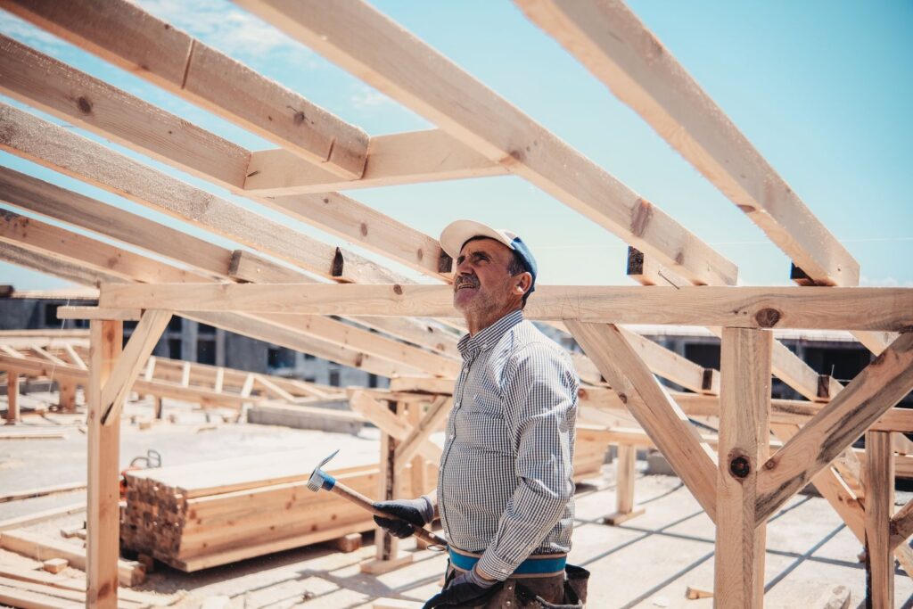 Builder in a cap inspecting a timber roof frame on a sunny construction site
