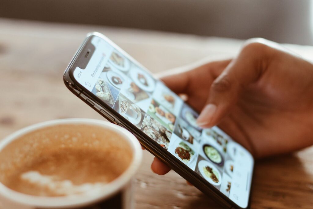 Person scrolling a social media feed on a phone next to a coffee, where facebook ads for builders are seen