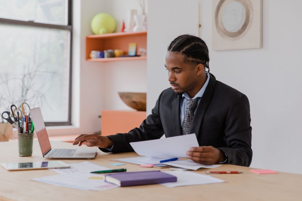 Business owner in a suit working through documents at his desk with a laptop open