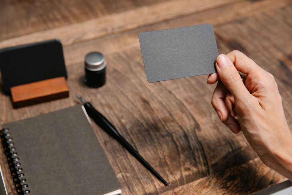 Hand holding a blank business card over a wooden desk, a reminder to keep business identity details consistent