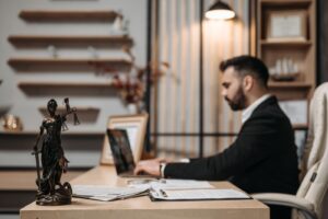 Lawyer working on a laptop at a desk with legal files and a Lady Justice statue