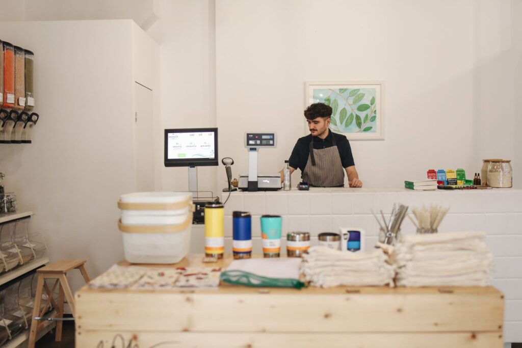 Small business owner standing behind the counter of his shop next to a computer