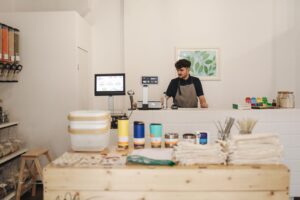 Small business owner standing behind the counter of his shop next to a computer